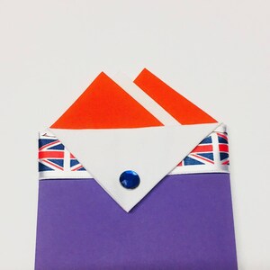 May include: A purple fabric envelope with a white flap and a Union Jack ribbon. The flap has a red and white folded fabric square inside. A blue jewel is centered on the flap.