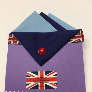 May include: A purple card with a blue and light blue triangle folded over the top. The triangle has a red button in the center. The card has a white sticker with a Union Jack flag and text that reads: "From: Hipster UK 38 West Street Dunstable Beds LU6 ITA Text only 07803 293693 www.hipsteruk.co.uk"