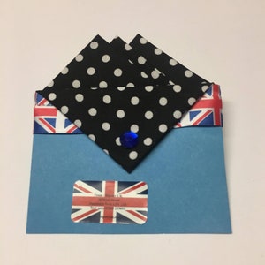May include: A blue envelope with a Union Jack design on the flap. The envelope contains three black and white polka dot fabric squares. A blue gem is attached to the fabric squares.