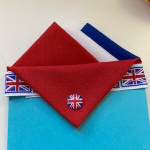 May include: A blue card with a red, white, and blue fabric triangle on top. The triangle has a button with a Union Jack design in the center. The card has a scalloped edge.
