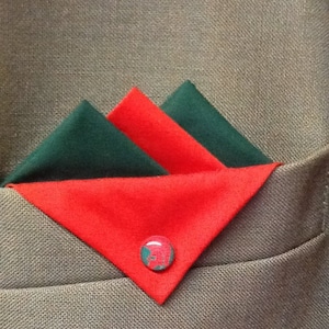 May include: A red and green pocket square with a red button in the center. The pocket square is folded into a triangle shape.