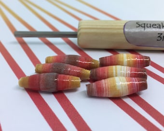 May include: Six colorful paper beads with a red, orange, and yellow striped pattern. The beads are arranged in a row on a white and red striped surface. The beads are made of paper and have a glossy finish.