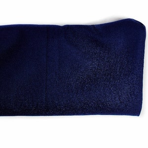 Puede incluir: Una diadema de tela azul marino oscuro con una textura suave y ligeramente reflectante. El material parece ser una mezcla sint&eacute;tica con un tejido fino y consistente. Un peque&ntilde;o logotipo azul y blanco es visible en la esquina inferior derecha.