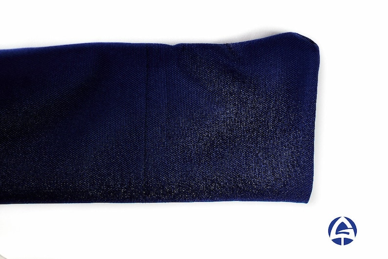 Puede incluir: Una diadema de tela azul marino oscuro con una textura suave y ligeramente reflectante. El material parece ser una mezcla sint&eacute;tica con un tejido fino y consistente. Un peque&ntilde;o logotipo azul y blanco es visible en la esquina inferior derecha.