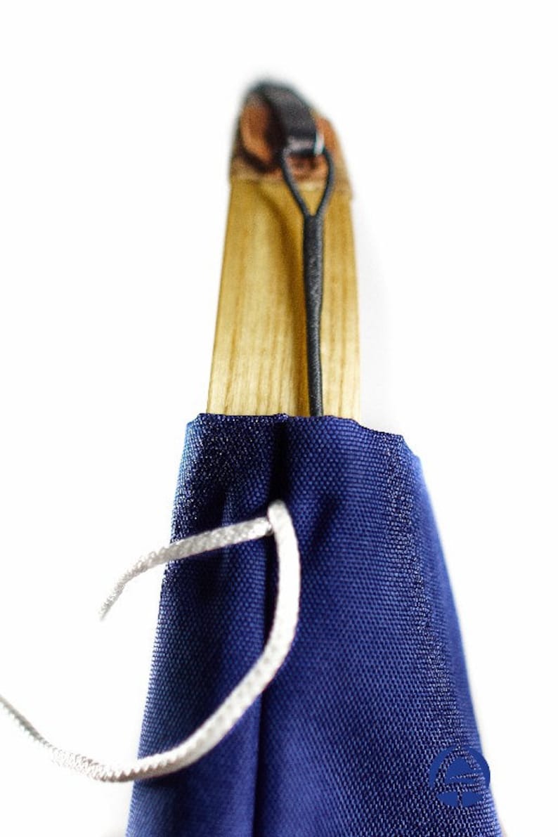 Puede incluir: Un mango de madera con veta marr&oacute;n claro est&aacute; parcialmente cubierto por una funda de tela azul oscuro. Un cord&oacute;n negro fino est&aacute; sujeto a la parte superior del mango y un hilo blanco atraviesa la tela cerca de la base de la madera.