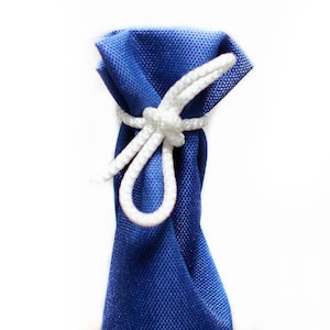 Puede incluir: Una bolsa de tela azul real con un tejido texturizado, cerrada en la parte superior con un cord&oacute;n trenzado blanco atado en un nudo simple. La bolsa est&aacute; orientada verticalmente sobre un fondo blanco liso y presenta un logo azul y blanco.