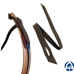 Puede incluir: Una correa de cuero marrón con un agujero, unida a un arco de madera. La correa está doblada y colocada sobre un fondo blanco.