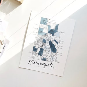 May include: A hand-drawn map of Minneapolis, Minnesota, with blue watercolor washes highlighting different neighborhoods. The map includes neighborhood names like Camden, Powderhorn, and North East. The text "Minneapolis, Minnesota" is written at the bottom of the map.