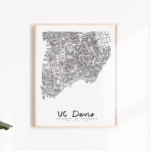 May include: A framed black and white map print of UC Davis. The map details the campus layout, with buildings and streets clearly illustrated. The text "UC Davis" is written in a handwritten style font, with the university's full name and location below.