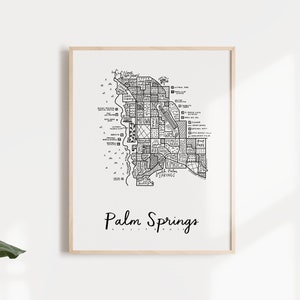 May include: A black and white line art print of a map of Palm Springs, California. The print is framed in a light wood frame and is hanging on a white wall.