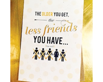 May include: A white card with black and gold text that reads "THE OLDER YOU GET, the less friends YOU HAVE... (how sad?)".  The card has a white background with small gold polka dots.  There are six stick figures with an X over them.