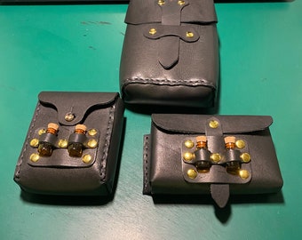 May include: Three black leather pouches with gold accents and buckles. Two of the pouches have small glass vials with cork tops inside.