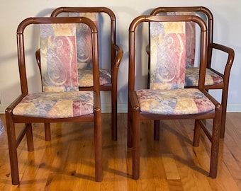 May include: Set of four wooden dining chairs with a colorful patterned fabric upholstery. The chairs have a simple, elegant design with a high back and arms.