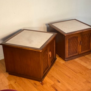 May include: Two wooden end tables with white marble tops and doors. The tables have a wood grain pattern and are in a mid-century modern style.