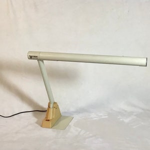 May include: A white desk lamp with a long, cylindrical arm. The lamp is made by the brand "Tenson" and has a white base with a black switch.
