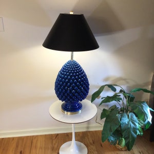 May include: A blue and black ceramic table lamp with a black lampshade. The lamp base is shaped like a pine cone and has a textured surface.