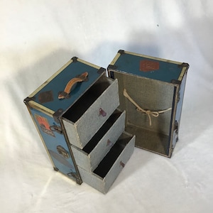 May include: A vintage blue and cream travel trunk with a leather handle and three drawers. The trunk is open and the drawers are pulled out, revealing a fabric lining.