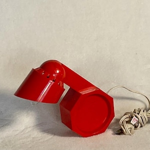 May include: A red desk lamp with a round base and a flexible arm. The lamp has a white cord.