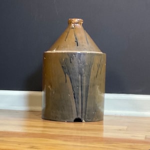 May include: A brown stoneware jug with black glaze and a spout. The jug has a rounded body and a narrow neck.