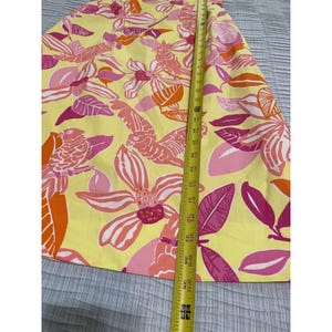 May include: A yellow skirt with a vibrant floral pattern in shades of pink, orange, and white. The skirt is measured with a tape measure, showing a length of approximately 36 inches.