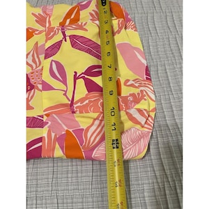 May include: Yellow fabric with a vibrant floral pattern in shades of pink, orange, and white. The fabric is measured with a tape measure, showing a width of approximately 11 inches.