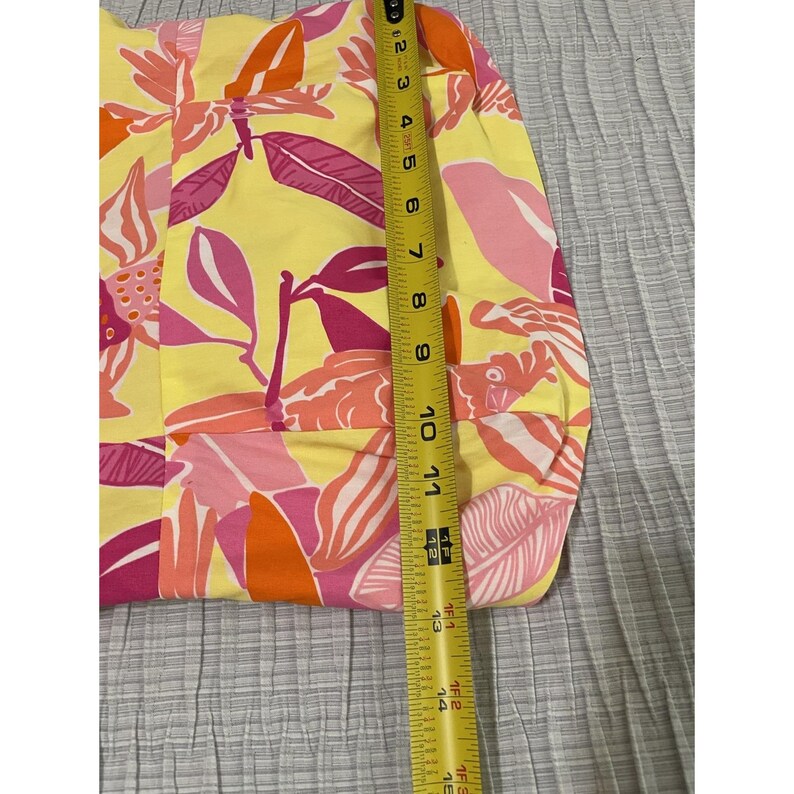 May include: Yellow fabric with a vibrant floral pattern in shades of pink, orange, and white. The fabric is measured with a tape measure, showing a width of approximately 11 inches.