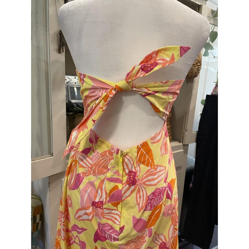 May include: A strapless yellow dress with a floral pattern in shades of pink and orange. The dress features a bow detail at the back and a zipper closure. The dress is displayed on a mannequin.