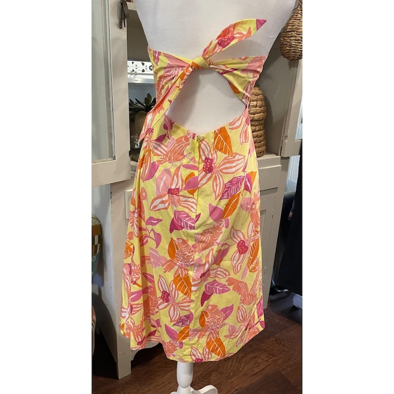 May include: A yellow floral print dress with a halter top and open back. The dress features a vibrant pattern of pink and orange flowers and leaves. The dress is tied at the back with a bow.