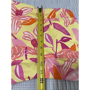 May include: A yellow fabric with a floral pattern in pink and orange. A measuring tape shows the fabric is approximately 12 inches long. The fabric has a repeating pattern of large flowers and leaves.