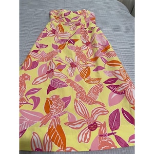 May include: A strapless yellow dress with a vibrant floral and bird pattern. The design features pink, orange, and white flowers and birds. The dress is made of a lightweight fabric, perfect for warm weather.