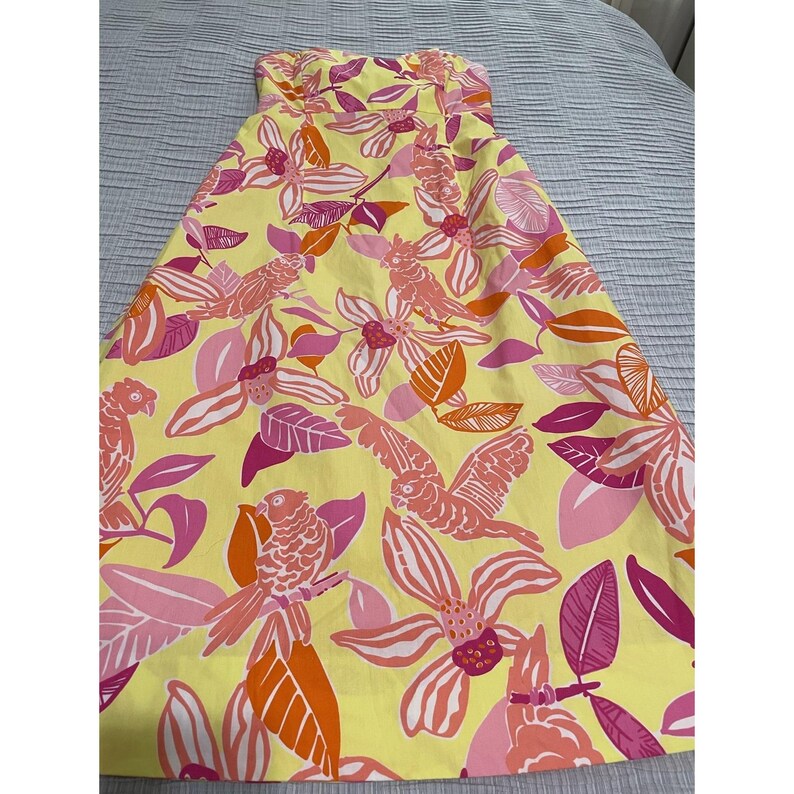 May include: A strapless yellow dress with a vibrant floral and bird pattern. The design features pink, orange, and white flowers and birds. The dress is made of a lightweight fabric, perfect for warm weather.