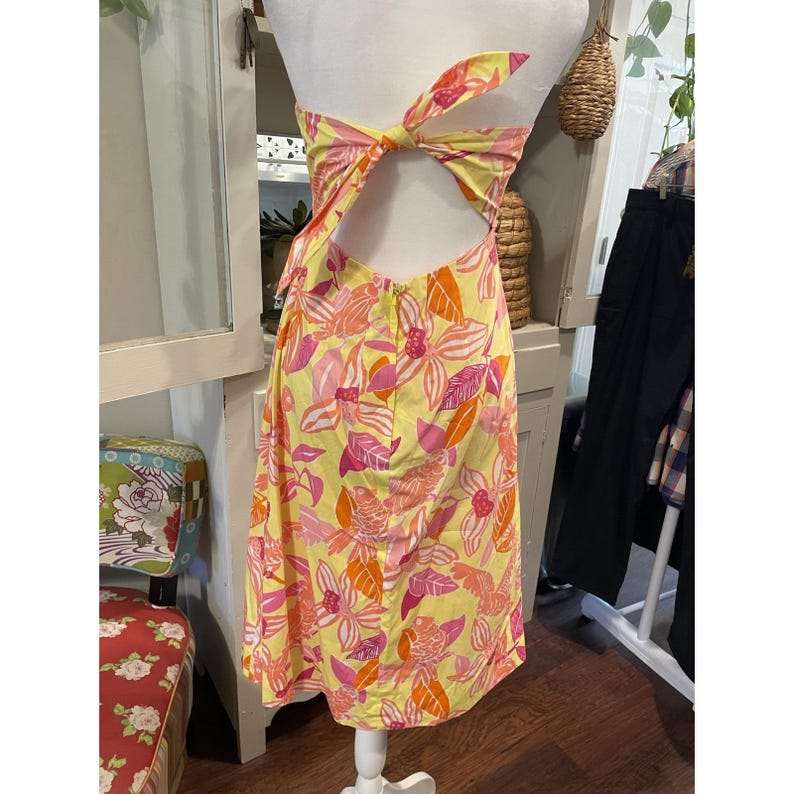 May include: A yellow sundress with a floral pattern in pink and orange. The dress has a halter top that ties in a bow at the back and a cut-out back design. The dress is displayed on a mannequin.