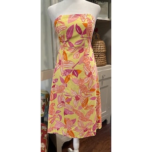 May include: A strapless, knee-length dress with a vibrant floral pattern. The dress features a yellow background with large pink, orange, and white flowers and leaves. The dress is displayed on a mannequin.