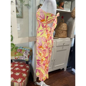 May include: A yellow, pink, and orange floral print dress on a white mannequin. The dress has a strapless top with a tie detail and a long skirt. The floral pattern includes large leaves and flowers.