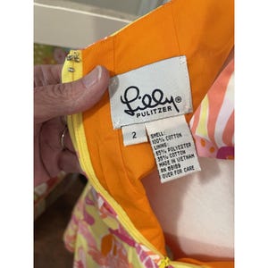 May include: Close-up of a colorful dress tag. The tag is white with the brand name "Lilly Pulitzer" in black script. The dress is size 2, made in Vietnam, and is composed of cotton and polyester.