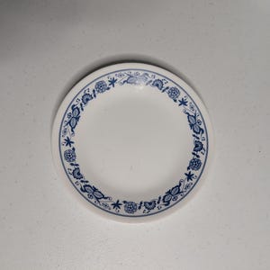 May include: White ceramic plate with a blue floral and leaf pattern around the rim. The plate has a simple, classic design, suitable for everyday use. The plate is round and appears to be about 8 inches in diameter.