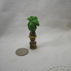May include: A green palm tree lamp finial with a gold base. The finial is about the size of a quarter.