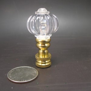May include: A clear glass finial with a ribbed design and a brass base. The finial is about the size of a quarter.