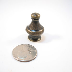 May include: A small, antique gold-toned finial with a bulbous shape and a decorative ring around the middle. The finial is about the size of a US quarter.