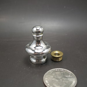 May include: A silver metal finial with a rounded top and a decorative base. The finial is about 2 inches tall and is shown next to a US quarter for size comparison.