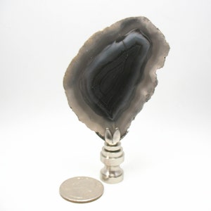 Peut inclure: Un embout de lampe en argent surmonté d'une tranche d'agate noire et blanche. La tranche d'agate a une forme naturelle et organique et présente un motif tourbillonnant de bandes noires et blanches.