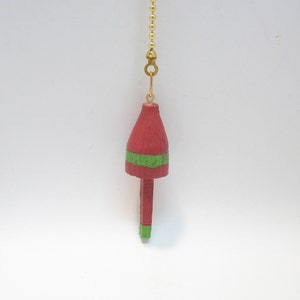 May include: A red and green wooden ceiling fan pull chain. The pull features a red buoy shape with a green stripe around the middle and green on the bottom. The pull is attached to a gold chain.