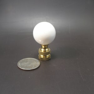May include: White ceramic lamp finial with a brass base. The finial is about the size of a US quarter.