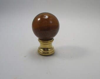 May include: A brown glass lamp finial with a gold metal base. The finial is round and has a smooth surface.