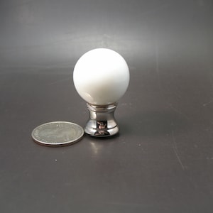 May include: A white, spherical lamp finial with a polished silver base. The finial is next to a U.S. quarter coin for size comparison. The lamp part is likely for a table lamp or floor lamp.