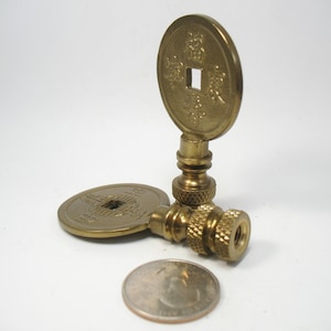 May include: Two gold-toned Chinese coin lamp finials with a square hole in the center of each coin. The finials are designed to be used as decorative lamp finials.