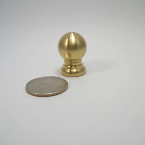 May include: A gold-colored metal finial with a rounded top and a fluted base. The finial is about the size of a US quarter.
