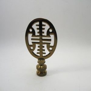 May include: A gold metal lamp finial with an intricate, geometric design. The finial is oval shaped and has a cut-out pattern.