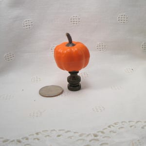 May include: A small orange pumpkin shaped lamp finial with a brown metal base.