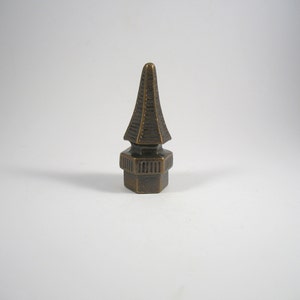 May include: A bronze finial with a pointed top and a hexagonal base. The finial has a decorative design with multiple layers.
